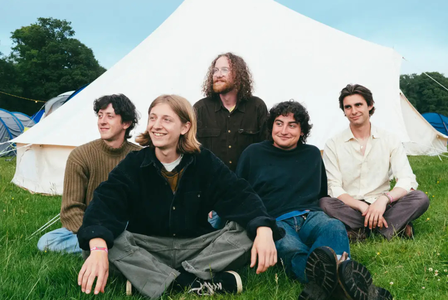 Band looking happy in front of a tent whilst touching grass